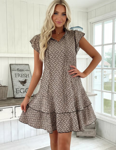 A woman wearing a brown printed V-neck dress with lace-up and flutter sleeves.
