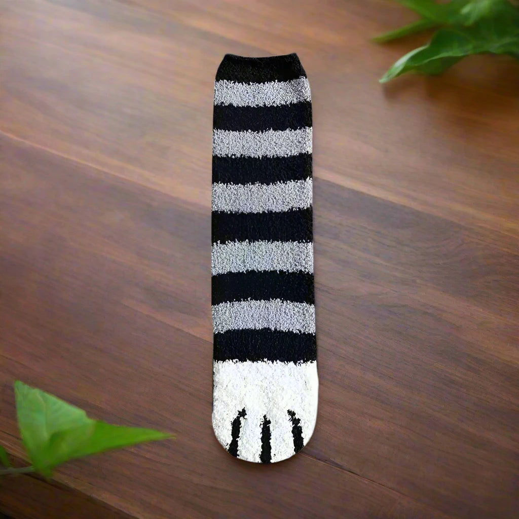 A pair of socks with a cat paw design, primarily in white with black and orange details, worn on a person's feet.