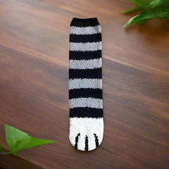 A pair of socks with a cat paw design, primarily in white with black and orange details, worn on a person's feet.