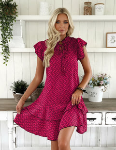 A woman wearing a red and black printed V-neck dress with lace-up and flutter sleeves.