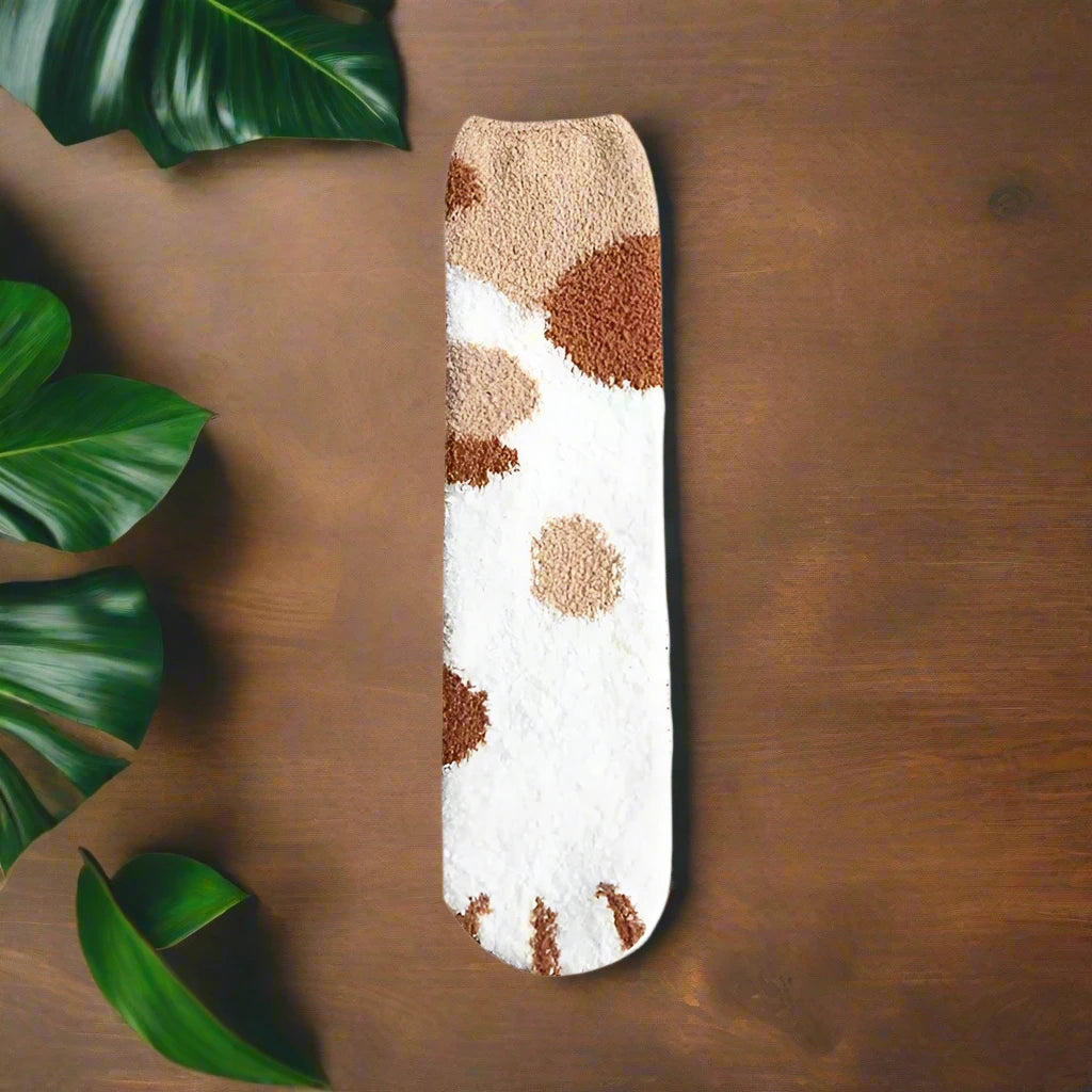 A pair of socks with a cat paw design, primarily in white with black and orange details, worn on a person's feet.