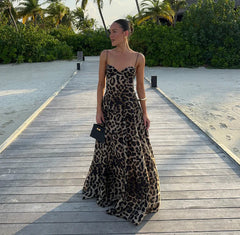 A person standing on a wooden pathway wearing a leopard print dress with a camisole neckline, sleeveless design, and a long skirt.