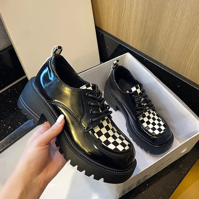 A pair of black and white checkered thick sole lace-up leather shoes presented on a box with a hand holding one shoe.