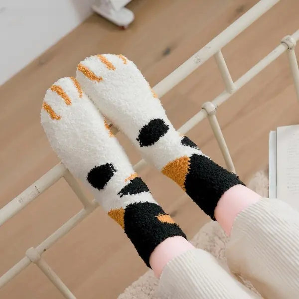 A pair of socks with a cat paw design, primarily in white with black and orange details, worn on a person's feet.