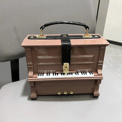 Pink piano-shaped jewelry box with a black strap on a white surface