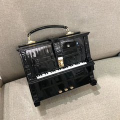 Black piano-shaped handbag with gold accents on a gray surface.