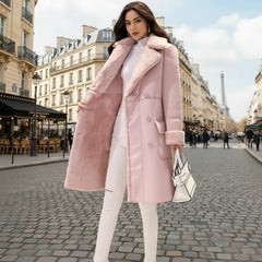 A woman wearing a long pink lambswool coat with a lapel collar, white top, and white pants, carrying a white handbag.