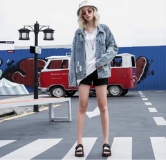 Person wearing a denim jacket and black shorts standing in front of a colorful mural.