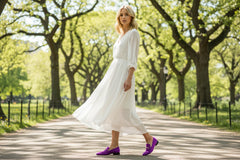 Purple loafers with gold buckles worn by a person on a white background