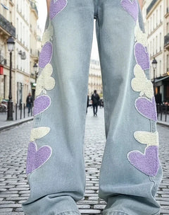 Person wearing light blue jeans with heart patterns on a city street.