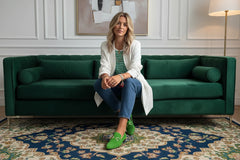 Person wearing green loafers sitting on a textured rug with a white coat and striped shirt.