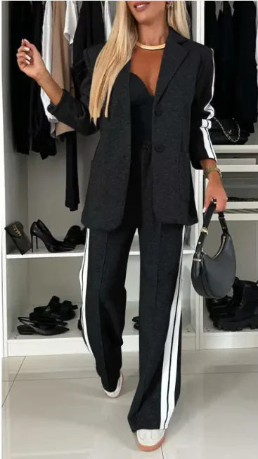 A woman modeling a black long sleeve suit with white side stripes on the pants, featuring a tailored lapel collar.