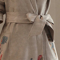 Close-up of a beige trench coat with floral embroidery on a neutral background