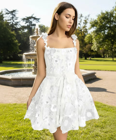 A woman wearing a white sheath dress with 3D floral embroidery and bow details on the straps.